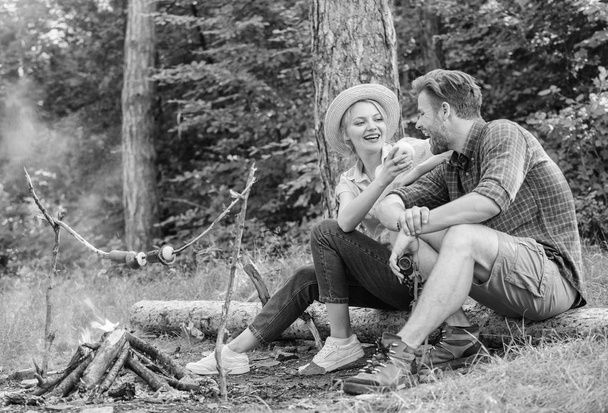 Couple relaxing sit on log having snacks. Family enjoy romantic weekend in nature. Girl offers eat apple while they waiting roasted food. Picnic roasting food over fire. Have snack. Cooking at picnic - Foto, immagini
