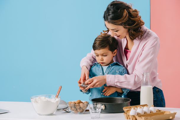 pretty mother with cute little son cracking walnuts while cooking together on bicolor background  - Photo, Image