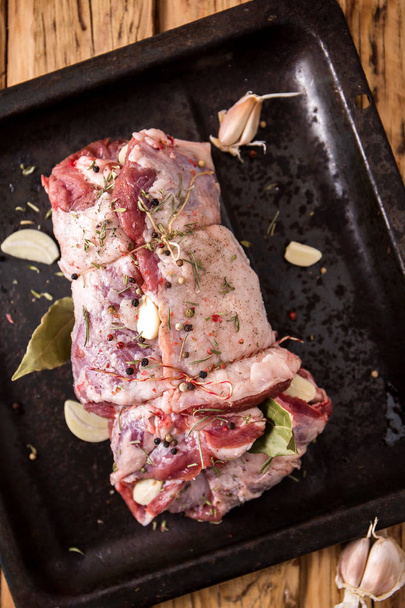rohes Fleisch mit Gewürzen umwickelt auf einem Backblech - Foto, Bild