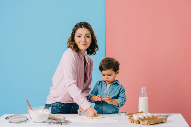 smiling mother kneading dough while cooking with little son together on bicolor background  - Valokuva, kuva