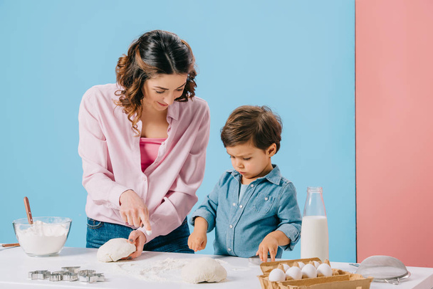 madre con poco lindo hacer pastelería en la mesa de cocina blanca sobre fondo bicolor
  - Foto, imagen