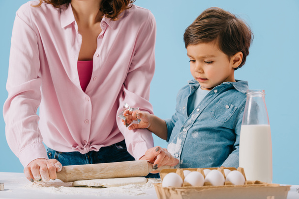 cute little boy watching mother rolling out dough isolated on blue - Photo, Image