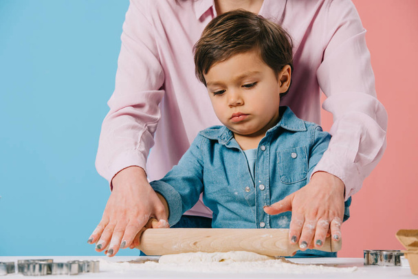 cute little boy rolling out dough together with mother on bicolor background - Fotó, kép