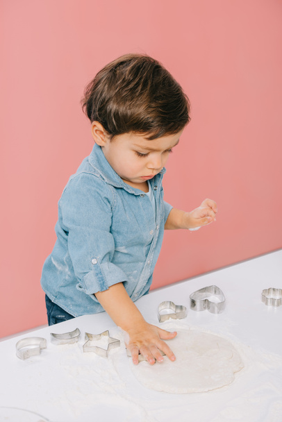 petit garçon découpe des figures dans la pâte avec des moules à pâte isolés sur rose
 - Photo, image