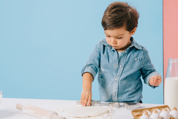 cute little boy diligently cuts figures in dough with dough molds on bicolor background - Fotó, kép