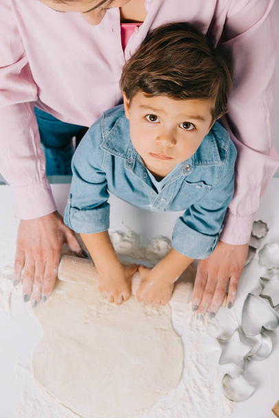 top view of cute little boy rolling out dough with mother on white background - Zdjęcie, obraz