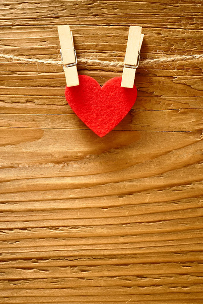 one red heart hanging on a rope with two pins in front of a brown wooden fence background. happy valentines day.  - Фото, зображення