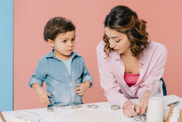 madre con lindo hijo pequeño pastelería de cocina juntos en la mesa de la cocina blanca sobre fondo bicolor
 - Foto, Imagen