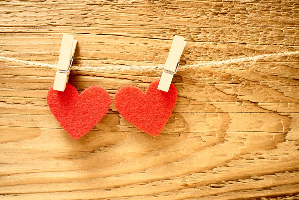  two red hearts hanging on a line in front of a brown wooden background. happy valentines day.  - Fotografie, Obrázek