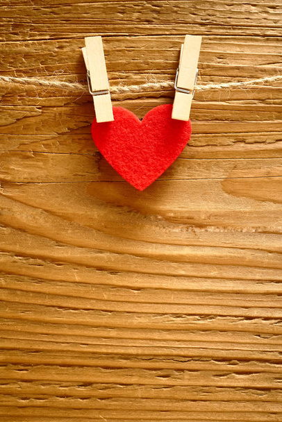 one red heart hanging on a rope with two pins in front of a brown wooden fence background. happy valentines day.  - Φωτογραφία, εικόνα