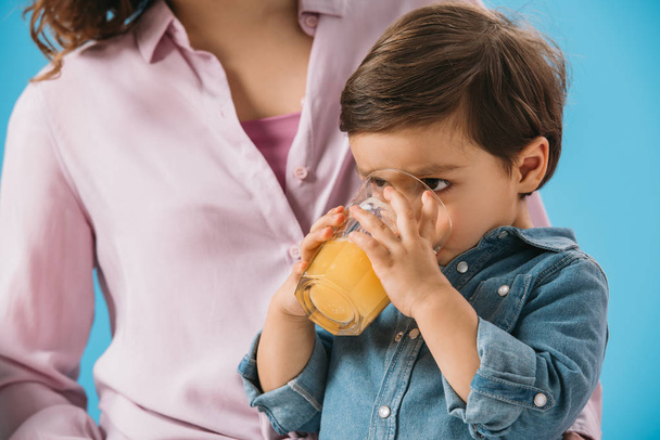 adorable little boy drinking fresh orange juice isolated on blue - Zdjęcie, obraz