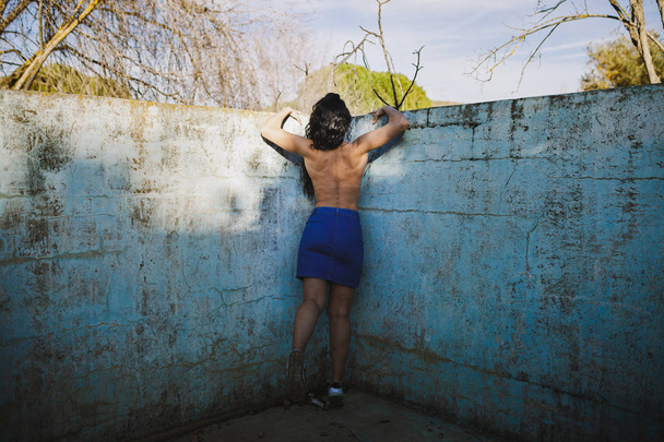 Linda morena contra a parede de uma piscina vazia despir-se com o sol iluminando suas costas nuas
 - Foto, Imagem