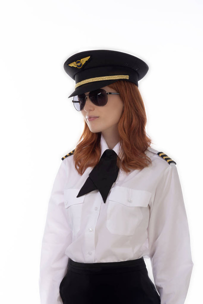 Νεαρή γυναίκα πιλότος με κόκκινα μαλλιά στέκεται στην αεροπορική εταιρεία στολή συμπεριλαμβανομένων ένα καπέλο - Φωτογραφία, εικόνα
