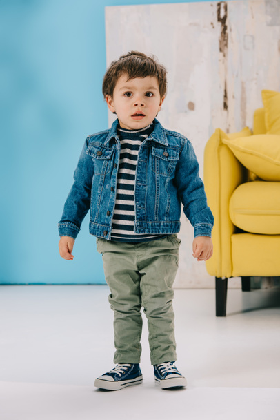 adorable little boy in blue jacket and green jeans standing in living room - 写真・画像