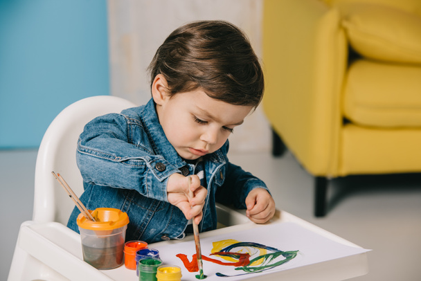 cute little boy painting with watercolor paints while sitting on highchair - Foto, Bild