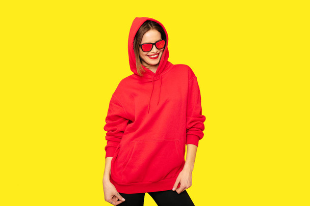 young and positive woman in red hoodie on yellow background - Foto, Imagem