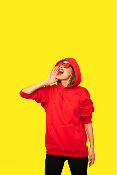 cool hipster girl with sunglasses screeming at someone, or protesting about something, in red hoodie - Fotoğraf, Görsel