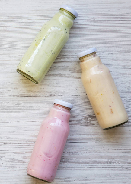 Fruit smoothies of different colors in glass bottles on white wooden surface. Top view, from above.  - Photo, Image