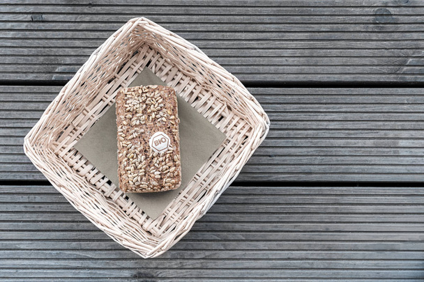 A loaf of bread lies in a beige basket on a wooden table. - Photo, Image