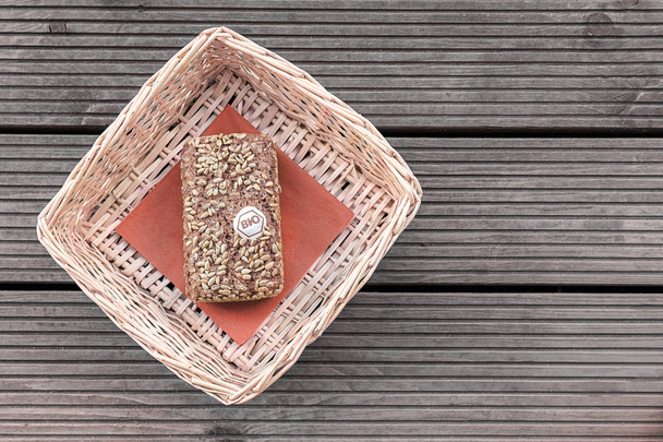 A loaf of bread lies on a red napkin in a beige basket on a wooden table. - Photo, Image
