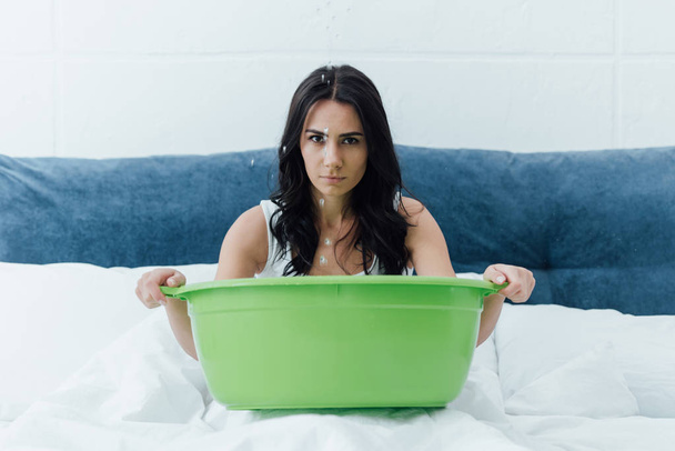 Sad girl with green basin dealing with leak in bedroom - 写真・画像