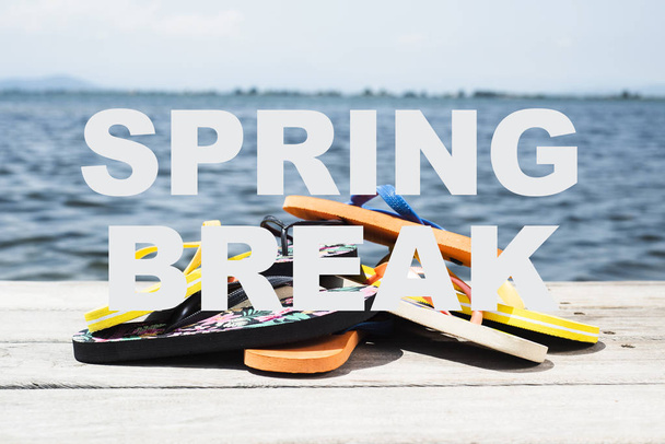 le spring break textuel et différentes paires de tongs sur une jetée en bois altérée, à côté de l'eau
 - Photo, image
