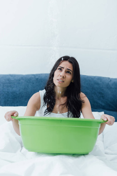 Boos brunette meisje holding groene bekken in bed en opzoeken - Foto, afbeelding