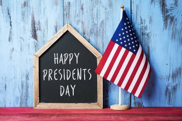 an american flag and a house-shaped chalkboard with the text presidents day written in it on a red wooden surface, against a blue wooden background - Photo, image