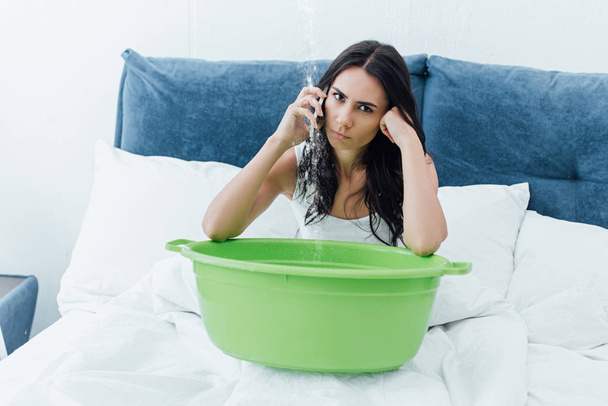 Irritált, barna nő beszél a smartphone, miközben ül ágyas, mosdóval - Fotó, kép