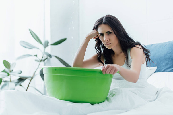 水漏れ時に洗面器が付いているベッドに座っている悲しい女性 - 写真・画像