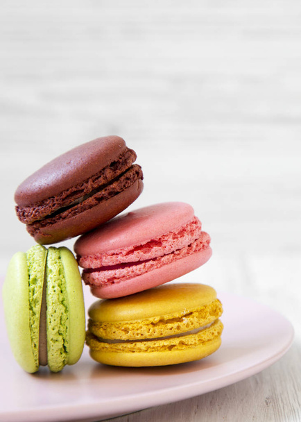 Sweet and colorful macarons on pink plate over white wooden background, side view. Closeup.  - Foto, Bild