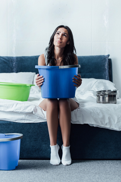 Upset woman in white socks holding bucket in bedroom - Photo, Image