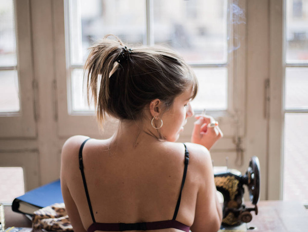 Bruneta žena ve spodním prádle, kouření a sedí v přední části ročník šicí stroj  - Fotografie, Obrázek