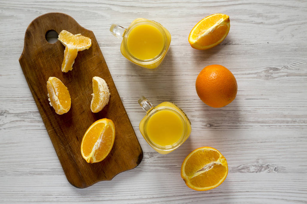 Jugo de naranja fresco en frascos de vidrio sobre superficie de madera blanca, vista superior. Puesta plana, desde arriba, sobre la cabeza
. - Foto, Imagen