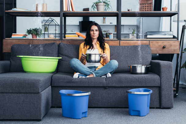 Beautiful woman with pots and buckets dealing with water damage in living room - Fotoğraf, Görsel