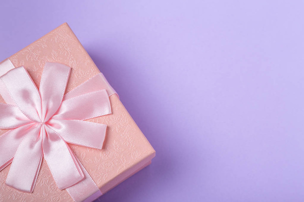 Розовая декоративная подарочная коробка с бантом на фиолетовом фоне с копировальным пространством
 - Фото, изображение