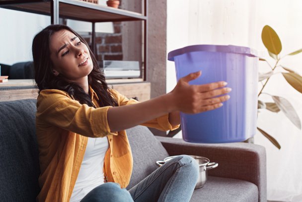 Naštvaná žena držící kbelík za unikající strop v obývacím pokoji - Fotografie, Obrázek