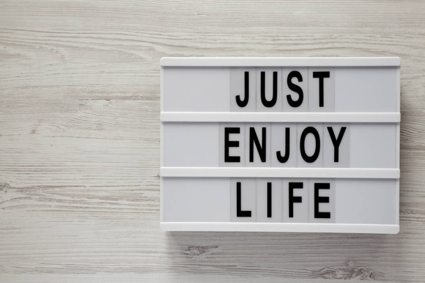 Modern board with text 'Just enjoy life' on a white wooden surface, top view. Space for text. - Фото, изображение