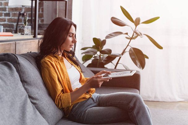 attraktive Frau im gelben Hemd sitzt auf Sofa mit digitalem Tablet - Foto, Bild