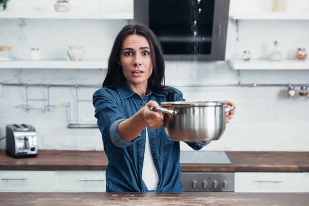 Amazed girl using steel pot during water leak in kitchen - Fotó, kép