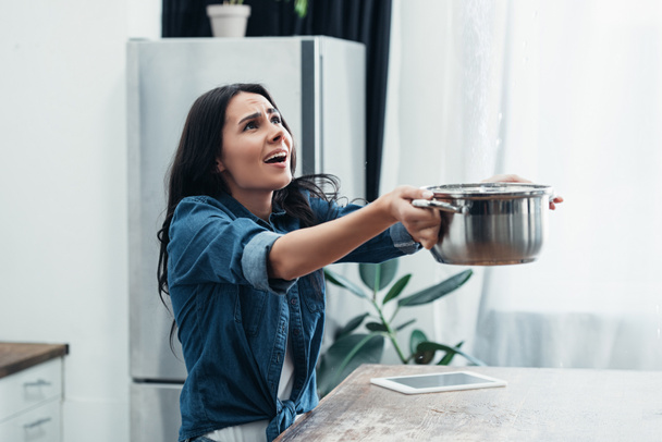 Worried woman in denim short with pot dealing with water damage in kitchen - Fotografie, Obrázek