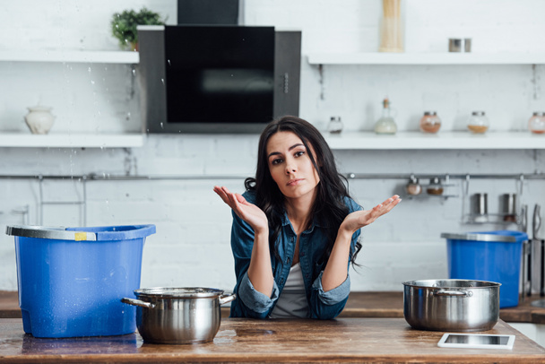 Brünette Frau bei Leck in Küche mit Töpfen und Eimern - Foto, Bild