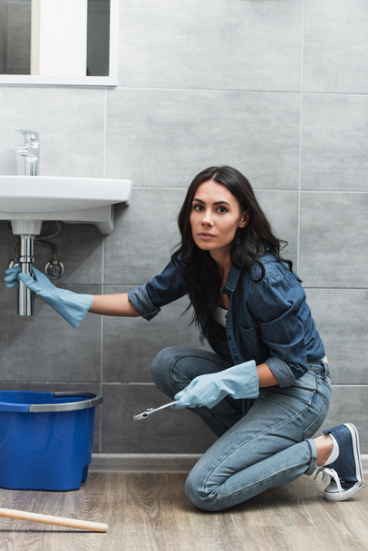 Serious woman in jeans reparing pipe in bathroom - Photo, Image