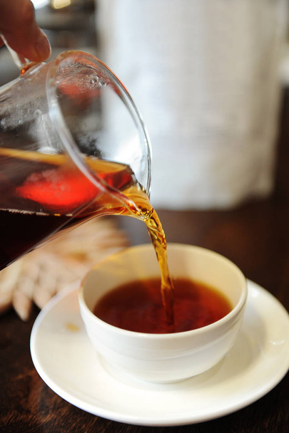 Pour freshly brewed black tea from a glass jug into a ceramic tea bowl - Fotoğraf, Görsel