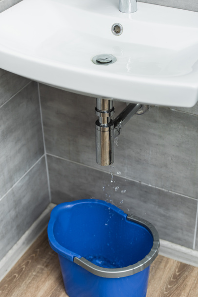 Sérült mosogató cső vízcseppek és kék vödör - Fotó, kép