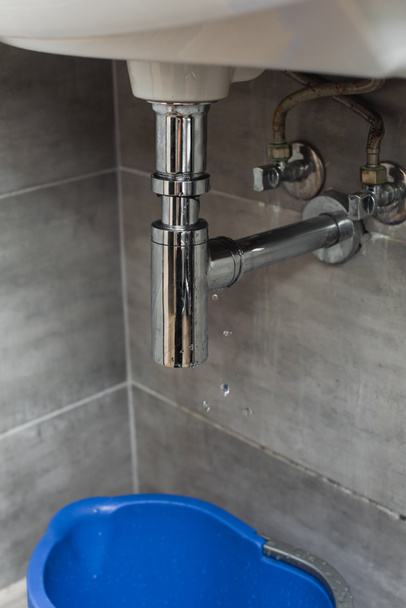 Blue bucket standing in bathroom under leaking pipe - Fotoğraf, Görsel