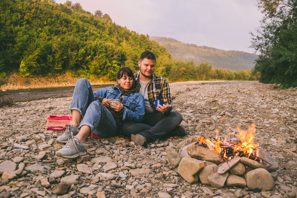 zwei junge Paare, die am Lagerfeuer sitzen, Tee trinken und sich unterhalten. Lifestylekonzept - Foto, Bild