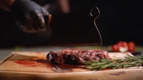 Male hand in black rubber gloves takes aim and chops meat lying on a cutting board with cutting knife close up. - Felvétel, videó