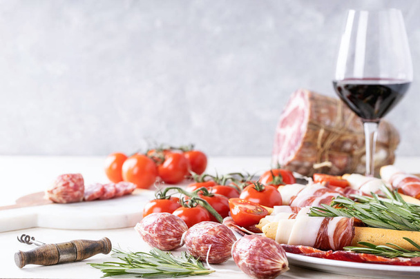 Selection of cured meats served with grissini, ham, salami, tomatoes, rosemary and red wine over white backround - Foto, Imagen