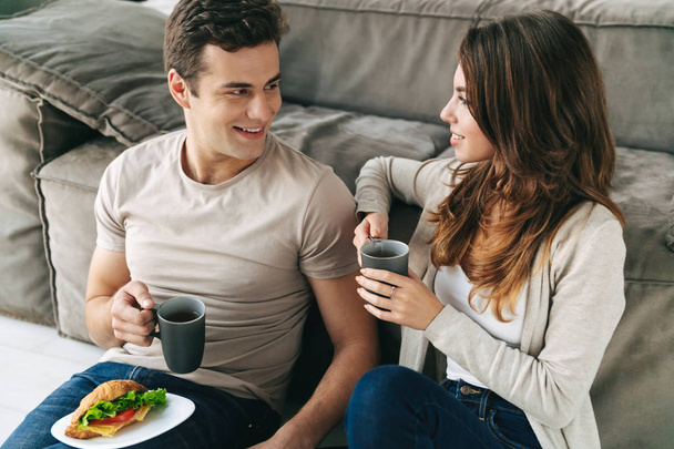 Šťastný usmívající se pár s ranní snídani v obývacím pokoji - Fotografie, Obrázek